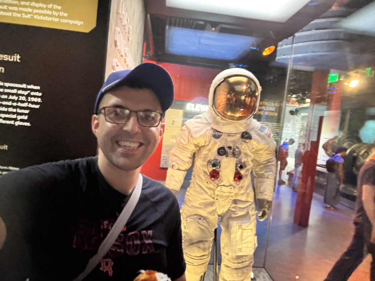 Sam Castillo smiling beside a NASA spacesuit in a museum exhibit